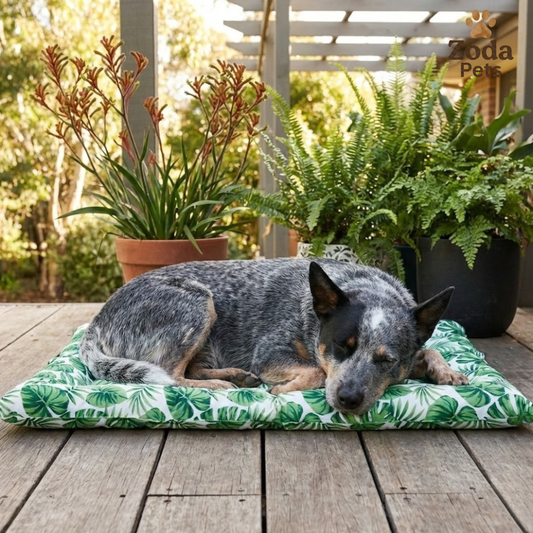 Dog lying on a green leaf-patterned cooling mat outdoors with plants in the background